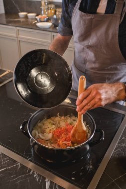 Gri önlüklü hasatçı fırının başında duruyor ve evde modern mutfakta yemek pişirirken domates sosunu erişteyle karıştırıyor.