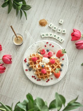 Masada böğürtlenli tatlı waffle 'ların üzerinde I Love Gofres yazıları ve açık mutfakta kahve var.