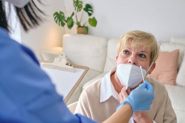 Tanınmayan pamuklu doktor COVID 19 için analiz yapmadan önce yaşlı bayanla solunum maskesi takıyor.