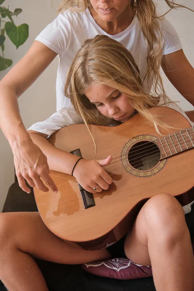 自宅のリビングルームでソファーに座ってギターで歌うように集中した女の子を教えるカジュアルな服の女性 — ストック写真