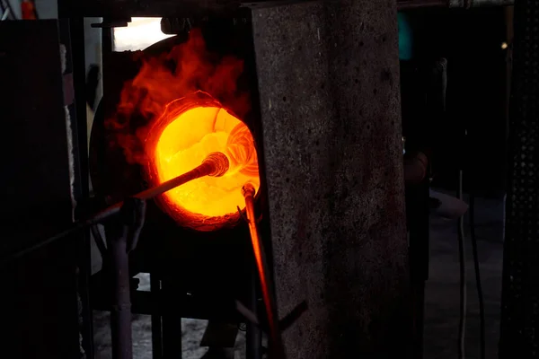 工場で燃える炎で炉に置かれた先端のホッカの花瓶の形の液体ガラスが付いているブローパイプ — ストック写真