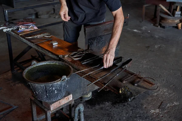 プロのガラス製造工場でワークベンチに配置するさまざまな金属工具で匿名の男性のガラスブロワーをクロップ — ストック写真