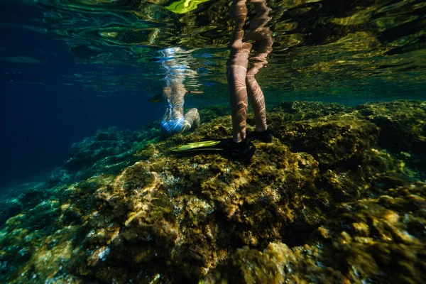 青い海でダイビング中に大規模な岩の形成に立って立って座っている水着とスリッパで認識できない男女のバックビュー — ストック写真
