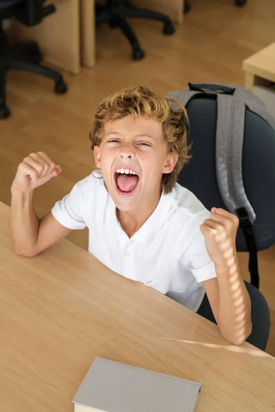 Joyful Schoolkid Celebrating Achievement While Sitting Clenched Fists Table Classroom — Stock Photo, Image