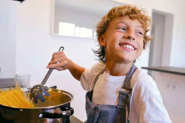 Χαρούμενο Παιδί Σπάτουλα Ζυμαρικών Μαγειρεύει Σπαγγέτι Κατσαρόλα Ενώ Κοιτάζει Αλλού — Φωτογραφία Αρχείου