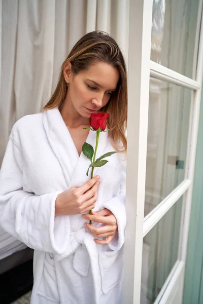 ホテルのスイートルームの窓に立っている間 赤い香りの白いテリーのバスローブを着用する思慮深い女性 — ストック写真