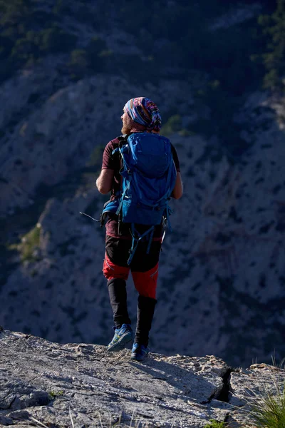 晴れた日には山の岩の斜面に立ってカジュアルな服のバックパックを持つ認識できないひげそりの男性ハイカーのバックビュー — ストック写真