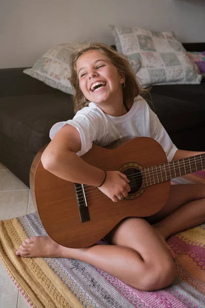カジュアルな服で幸せな子供は 週末の家でリビングルームでアコースティックギターを演奏しながら笑って遠ざけます — ストック写真