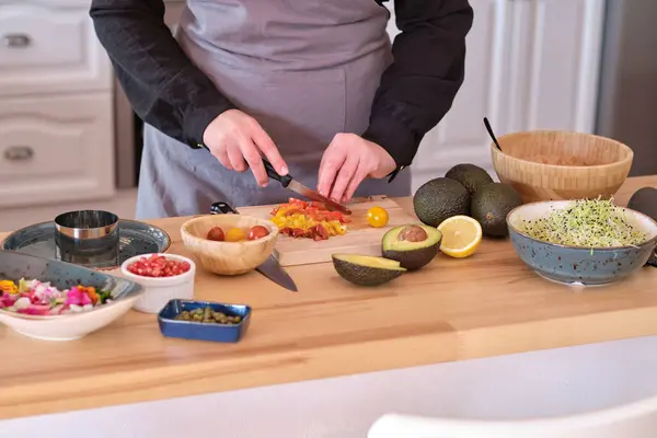 まな板でトマトを切る作物の認識できないシェフは キッチンで様々な成分とテーブルでおいしいタルタル料理を調理しながら — ストック写真