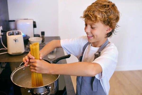 Content Child Putting Uncooked Pasta Saucepan Boiling Water Hob House — Stock Photo, Image