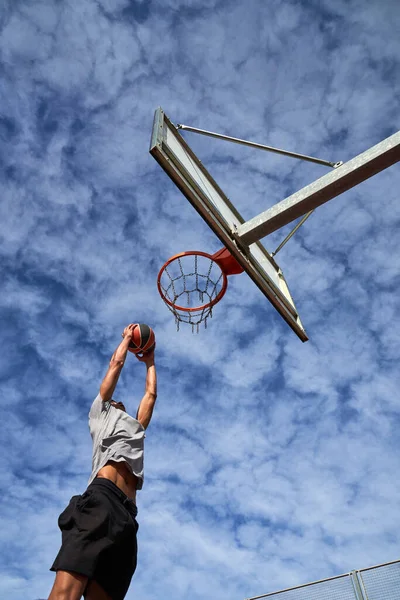 浅谈在蓝天的运动场上打篮球时 男子无脸强者在运动服投球中的低视角 — 图库照片