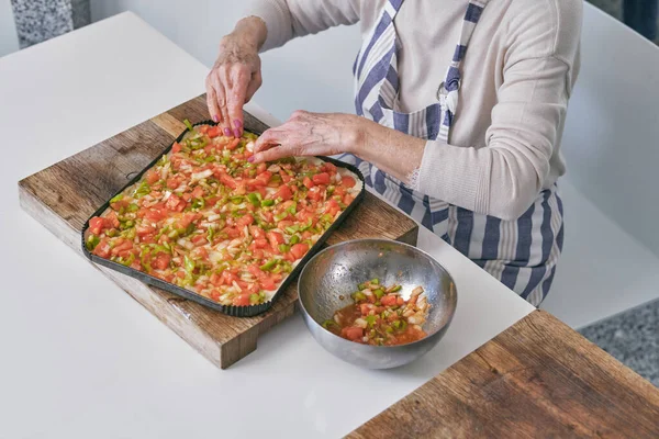 エプロンの匿名の女性チーフの上から 新鮮なカット野菜がいっぱいのボウルでテーブルに座っている間 切削ボードでピザを調理する — ストック写真