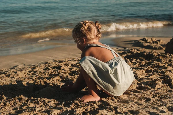 阳光明媚的日子里 穿着休闲装的小女孩在海浪的海滩边玩沙子 — 图库照片