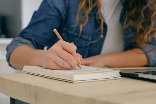 テーブルに座って宿題をしながらノートにメモを取るカジュアルな服の女性学生 — ストック写真