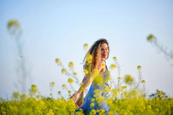 サイドビュー咲く芝生の上に立って青いサンドレスで若い女性を笑顔と幸せな夏の日にカメラを見て — ストック写真