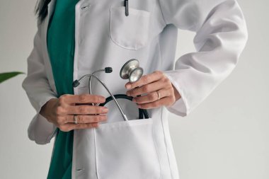 Tıp üniformalı tanınmayan bir kadın doktor steteskobu cebine koydu.