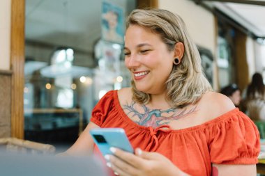 Açık havada çalışırken laptopla masada oturan, günlük giysiler içinde gülümseyen genç bayan serbest yazar portresi.