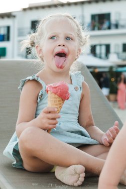 Açık tenli, kirli, çıplak ayaklı bir çocuk yazın meyveli şerbet külahının tadını çıkarırken uzanır ve başka yere bakar.