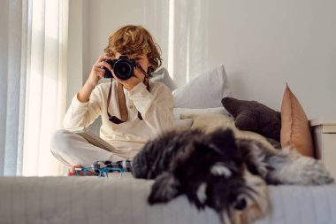 Bacak bacak üstüne atmış isimsiz bir çocuk profesyonel kamerada Minyatür Schnauzer 'e karşı evde fotoğraf çekiyor.