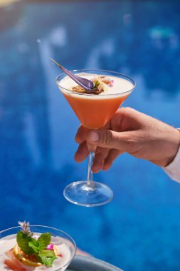 Bulanık arka planda çiçek yaprağı ile süslenmiş bir bardak taze kokteyl ile tanınmayan biri.