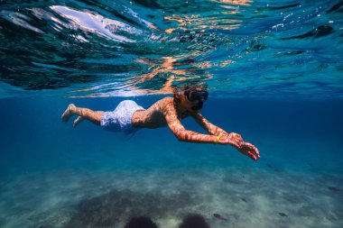 Tatil sırasında deniz suyunun altında yüzen, şnorkel maskesi takmış, tüp takmış genç bir çocuğun tüm vücudu kenar manzaralı.