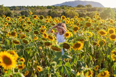Güneşli bir günde kırsalda çiçeklerle çiçek açmış sıradan giyinmiş mutlu bir çocuk.