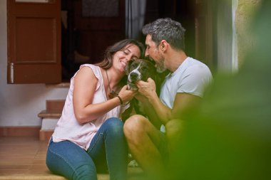 Gülümseyen kadın ve gözleri kapalı adam evin yakınındaki merdivenlerde oturup itaatkar köpeği okşarken eğleniyorlar.