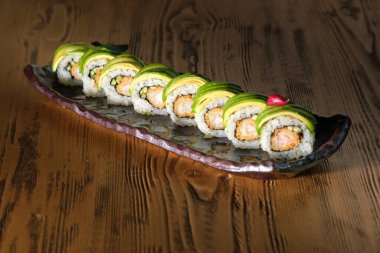 Lezzetli suşi rulolarının yukarısından avokado ve mermer tabakta karides ahşap masaya konur.