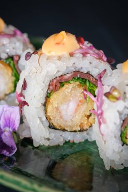 Karides ve soslu taze Japon suşisi mermer tabakta servis ediliyor ve siyah arka planda çiçek var.