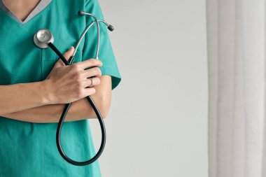 Kadın doktor, kolları katlanmış ve steteskopla arka planda.