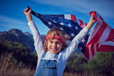 Neşeli gülümseyen çocuk bandanalı ve güneşli bir günde Amerikan bayrağı sallayan.