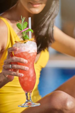 Sarı mayo giymiş, limonlu ve naneli taze kokteylli, bulanık arkaplanlı, isimsiz bir kadın.