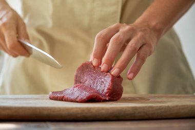 Profesyonel kadın aşçı mutfakta yemek pişirirken bıçakla et kesiyor.