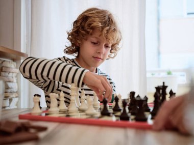 Odaklanmış çocuk portresi ahşap masada oturuyor ve evdeki mutfaktaki masada mahsullerle satranç oynamayı öğreniyor.