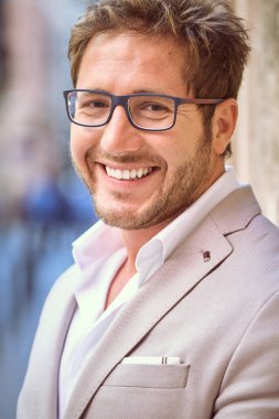 Zarif takım elbiseli ve gözlüklü bir girişimci bulanık arkaplanda kameraya bakıyor.