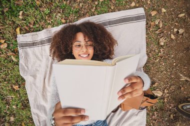 Afro saç stili siyahi bir kadının ilginç bir hikaye okuması ve doğada çimenlerin üzerinde dinlenirken gülümsemesi.