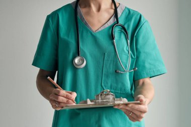 Yeşil üniformalı, cebinde steteskobu olan kimliği belirsiz kadın doktor.