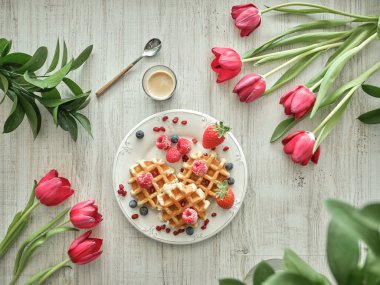 Masada kahve ve açık mutfakta kırmızı lalelerle servis edilen olgun böğürtlenli lezzetli waffle 'lardan.