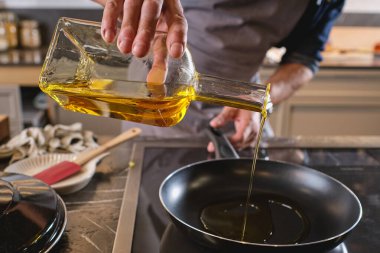 Anonim erkek aşçı hafif mutfakta tezgahta yemek pişirirken şişeden tavaya yağ döker.