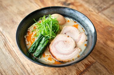 Yüksek oranda taze iştah açıcı ramen çorbası kremalı çorba ve domuz eti dilimleri ahşap masada servis edilir ve yeşilliklerle süslenir.