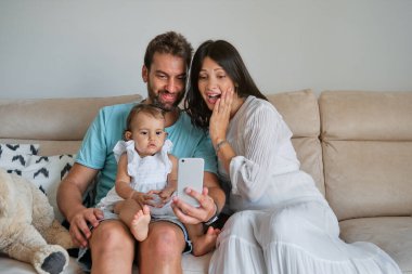 Mutlu adam ve kadın kanepede oturup akıllı telefondan video izliyorlar ve evde vakit geçiriyorlar.