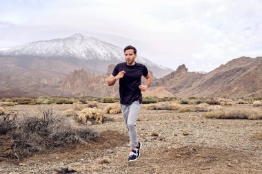 Tam boy odaklı sakallı İspanyol erkek sporcu dağ kıyısında kuru arazi boyunca koşuyor ve İspanya 'nın Tenerife Kanarya Adaları' na bakıyor.