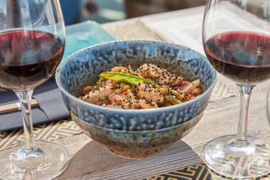 Kırmızı şarap kadehlerinin arasına konmuş geleneksel kasede servis edilen iştah açıcı ton balıklı susamlı ve sebzeli Japon yemeği.