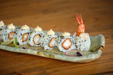 İştah açıcı California maki rulolarından karides ve sosla süslenmiş seramik tepside ahşap masaya konmuş.