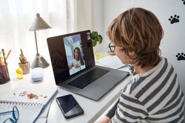 Evde ışık odasında ödevlerini yaparken dizüstü bilgisayardaki çocuk videosunun yan görüntüsü.