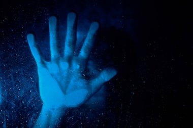 Tanınamayacak kadar yalnız, çaresiz biri mavi ışıkta saf su damlacıklarıyla cam duvara dokunuyor.