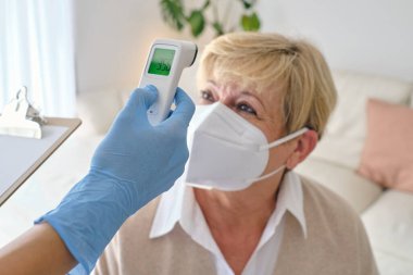 Lazer termometreyle solunum maskesi takan tek kullanımlık eldiven giyen kimliği belirsiz doktor.