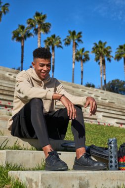 Spor kıyafetleri giymiş, yaz günü elinde su şişesiyle taş basamaklarda oturan İspanyol erkeklerinden oluşan bir vücut.