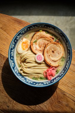 Lokantada güneş ışığı altında ahşap masaya konmuş ramen denen lezzetli erişteli kasenin en üst görüntüsü.