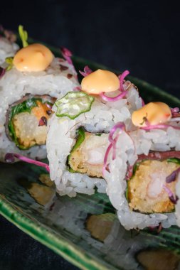 İştah açıcı uramaki rulolarının yukarısından siyah arka planda mermer tepside servis edilen sos ile servis edilir.